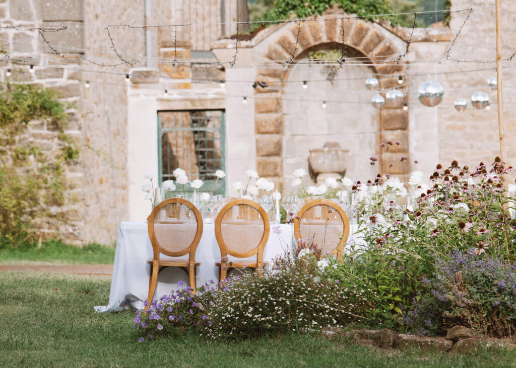 Al fresco wedding reception with white roses, natural wood chairs, and a lush garden