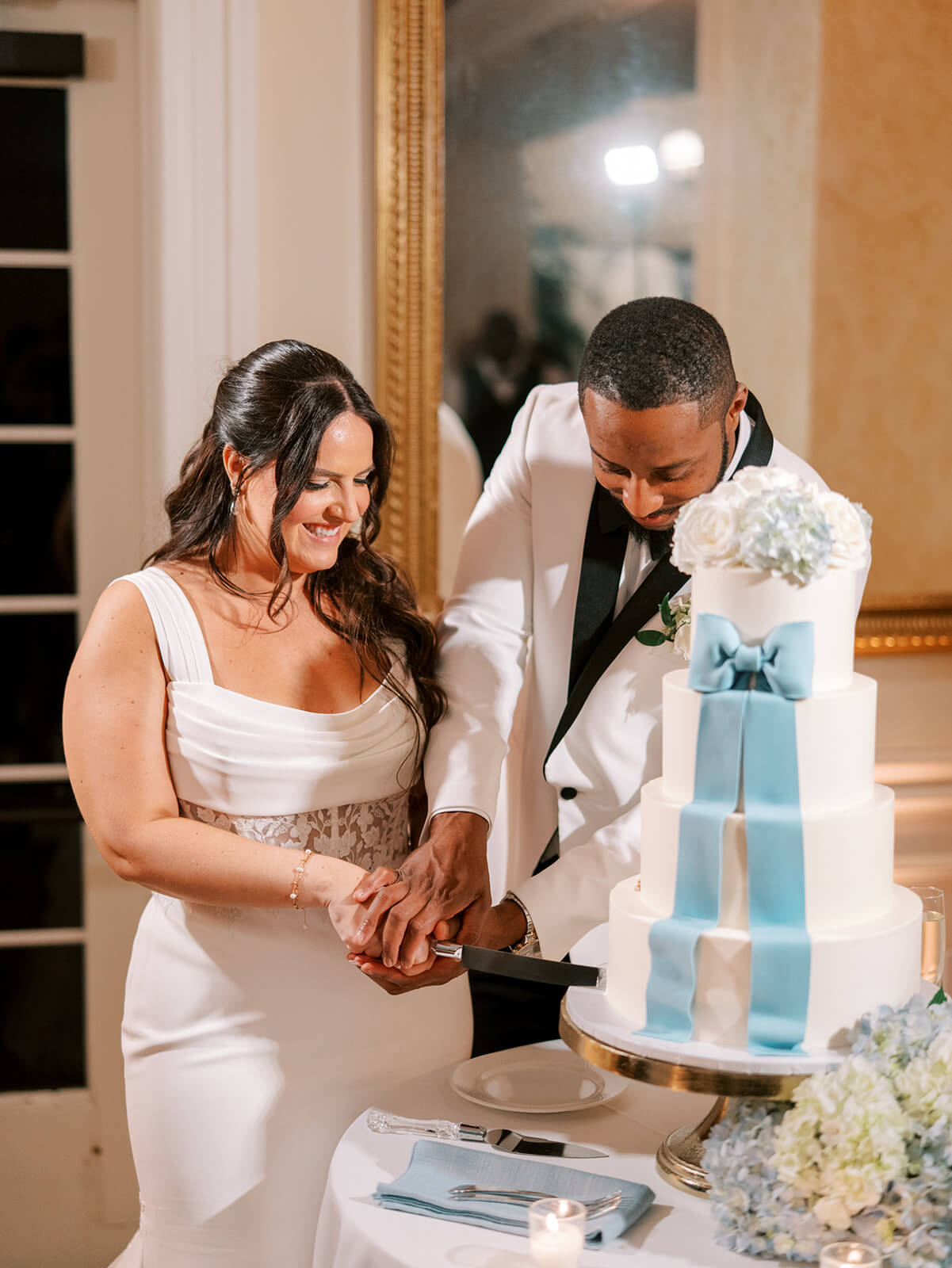 Bride and groom cut four-tiered wedding cake adorned with a blue ribbon
