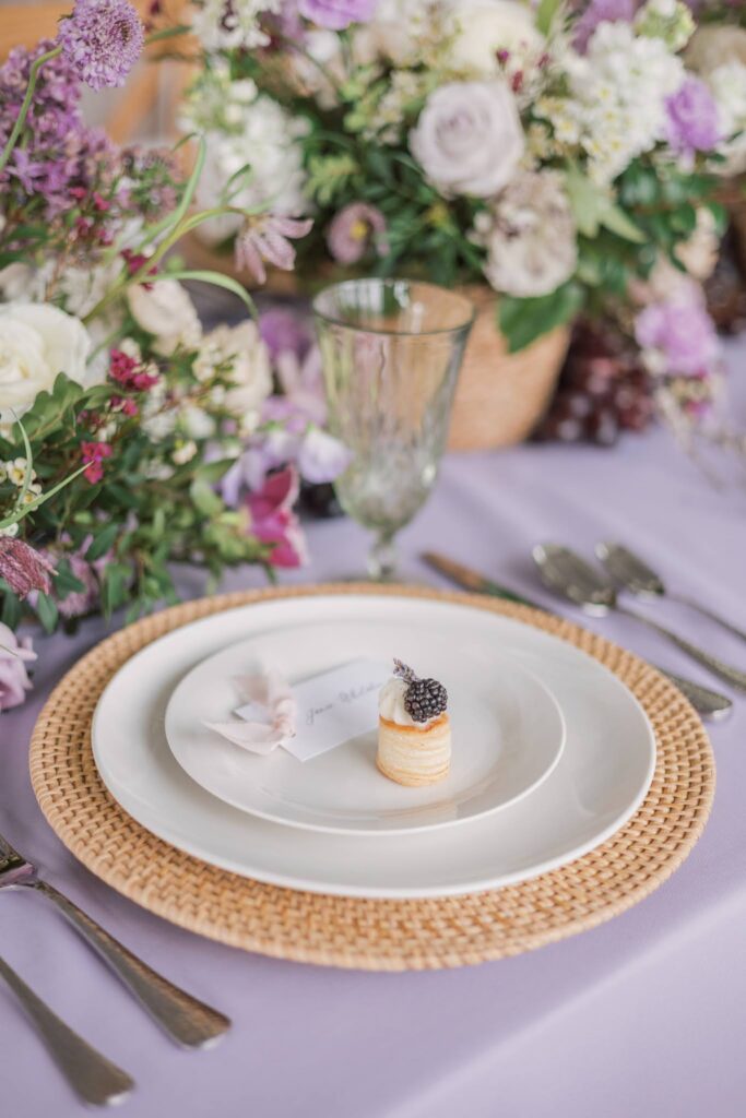 Purple table linen with a woven rattan charger and delicate place card