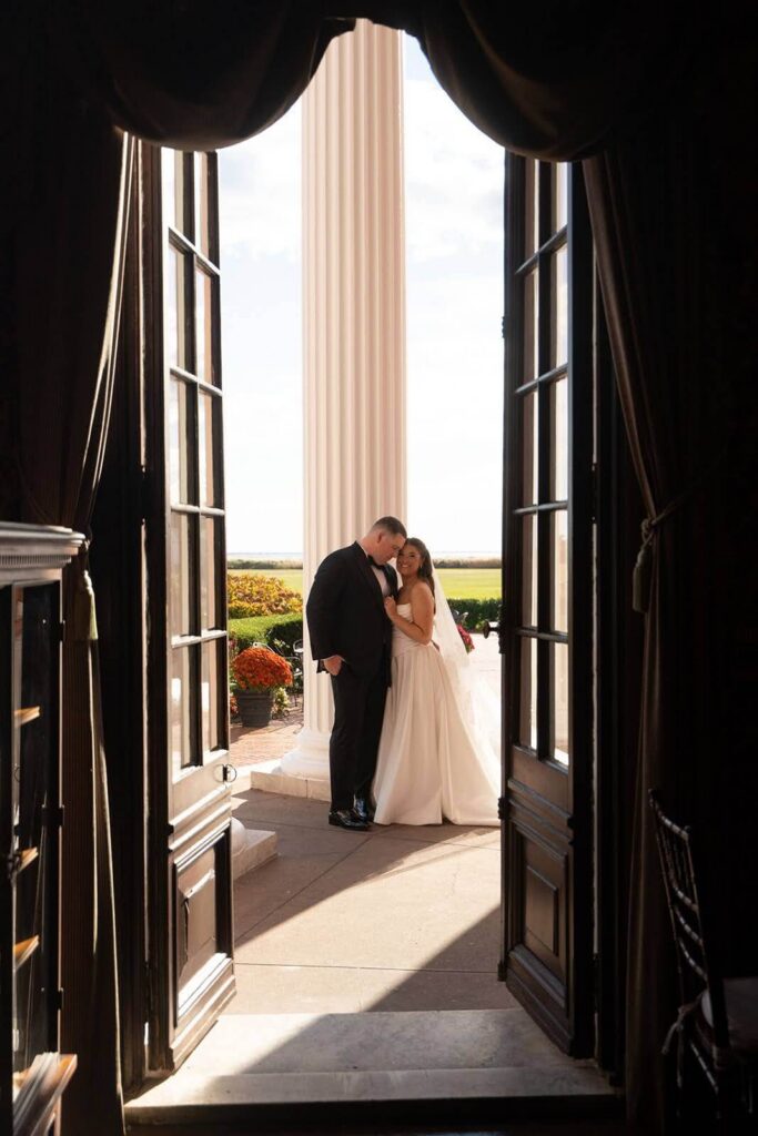Portrait of bride and groom through the French doors that open to a veranda