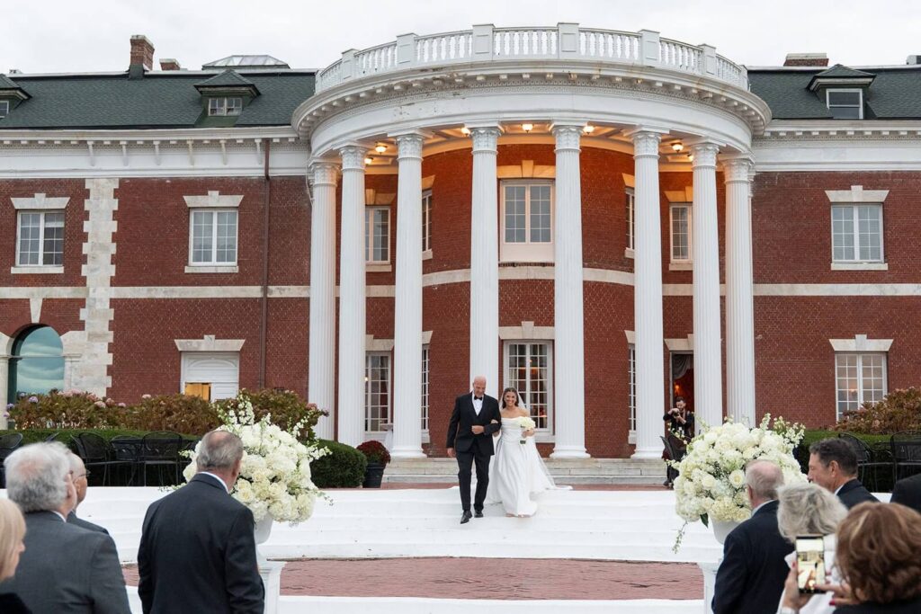 Bride and father walking down the aisle with Bourne Mansion in the background