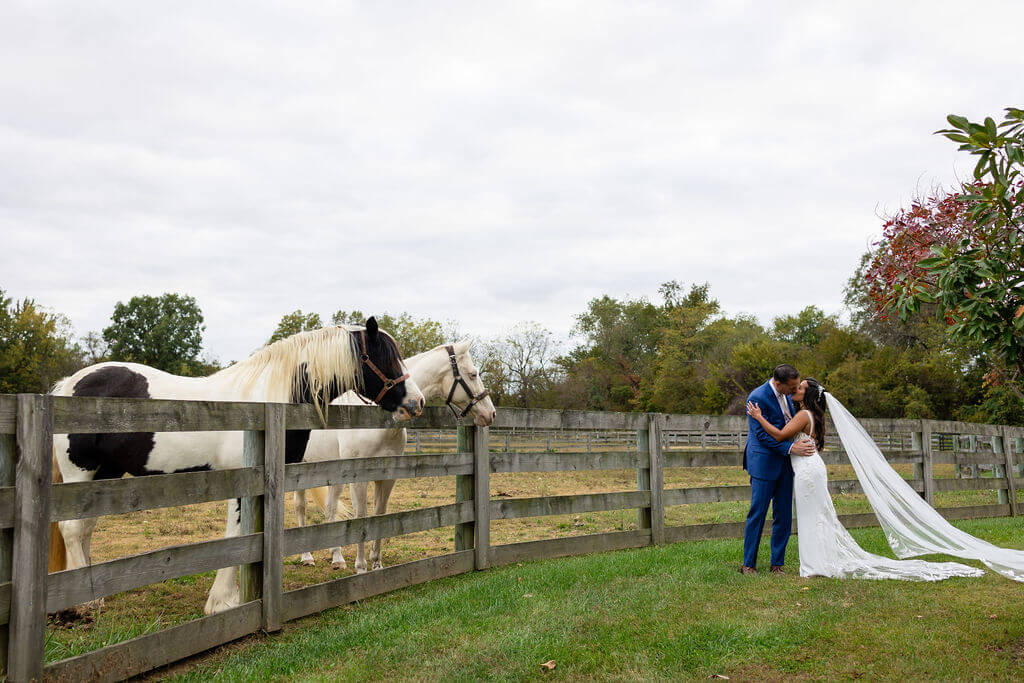 Bride and groom kissing as horses watch at Cecil Creek Farm