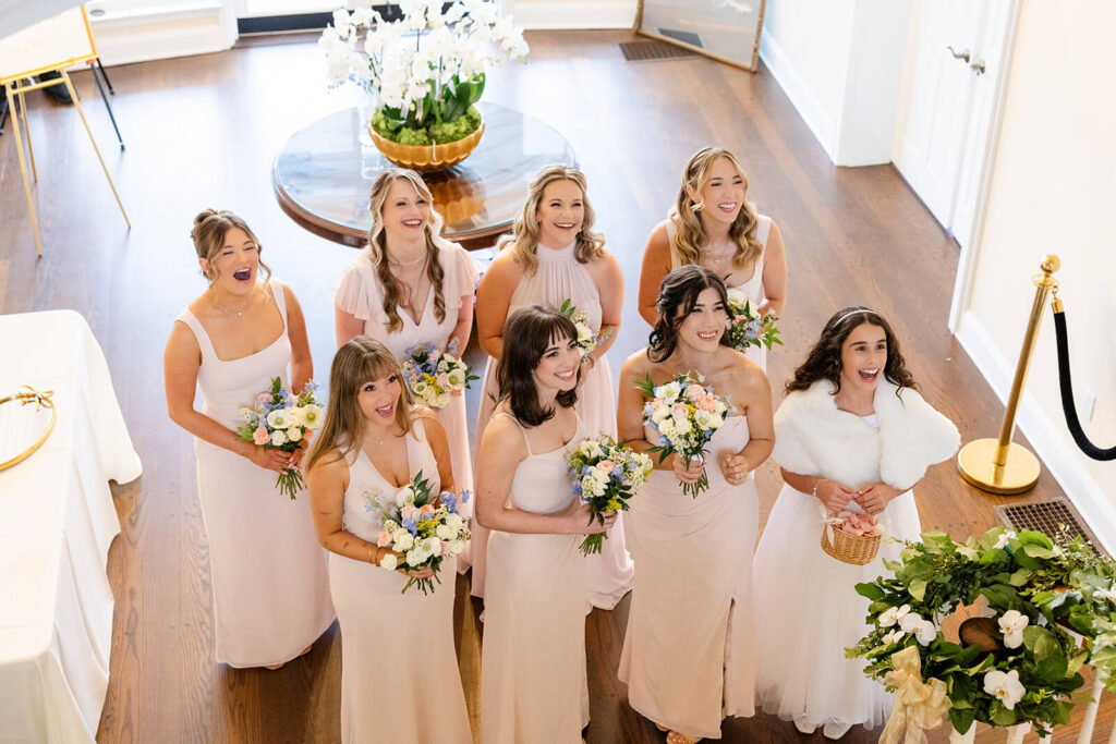 Bridesmaids dressed in light pink smile as they see the bride on her wedding day
