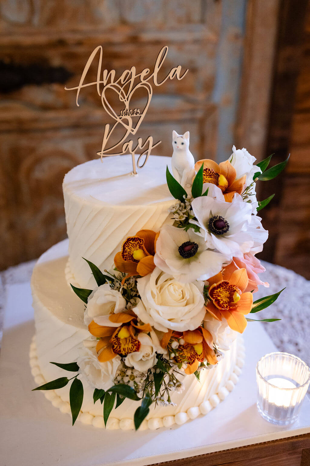 Two-tiered buttercream wedding cake with rustic flowers and a cat figurine