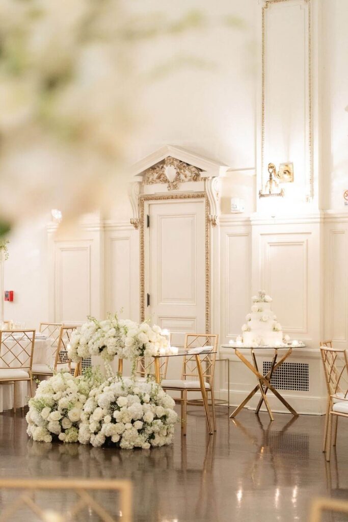 Elegant white and gold wedding reception sweetheart table with large floral arrangements