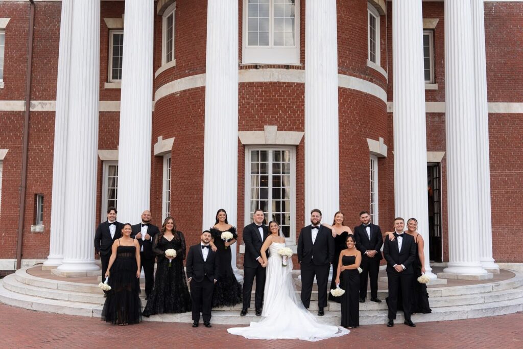 Wedding party, dressed in all black, outside Bourne Mansion with the bride and groom