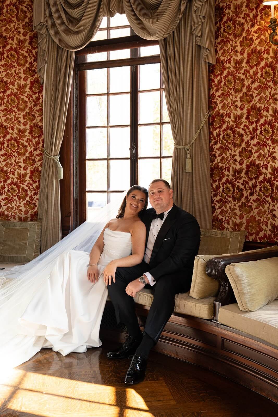 Portrait of couple sitting in the drawing room on their wedding day at Bourne Mansion