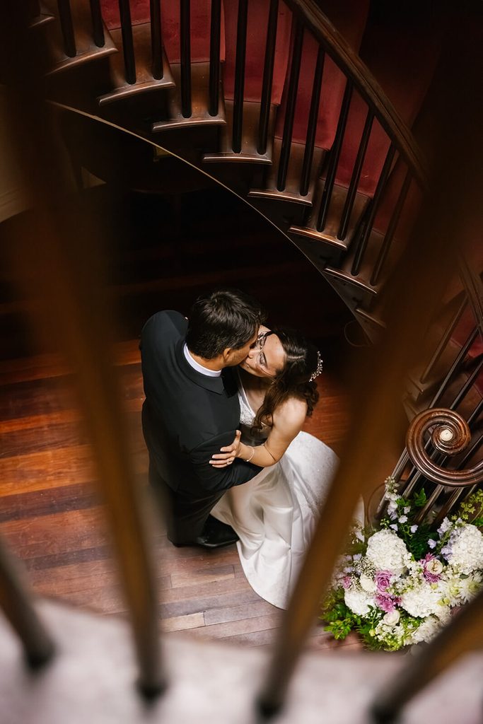 Bride and groom kissing at the bottom of a stunning spiral staircase