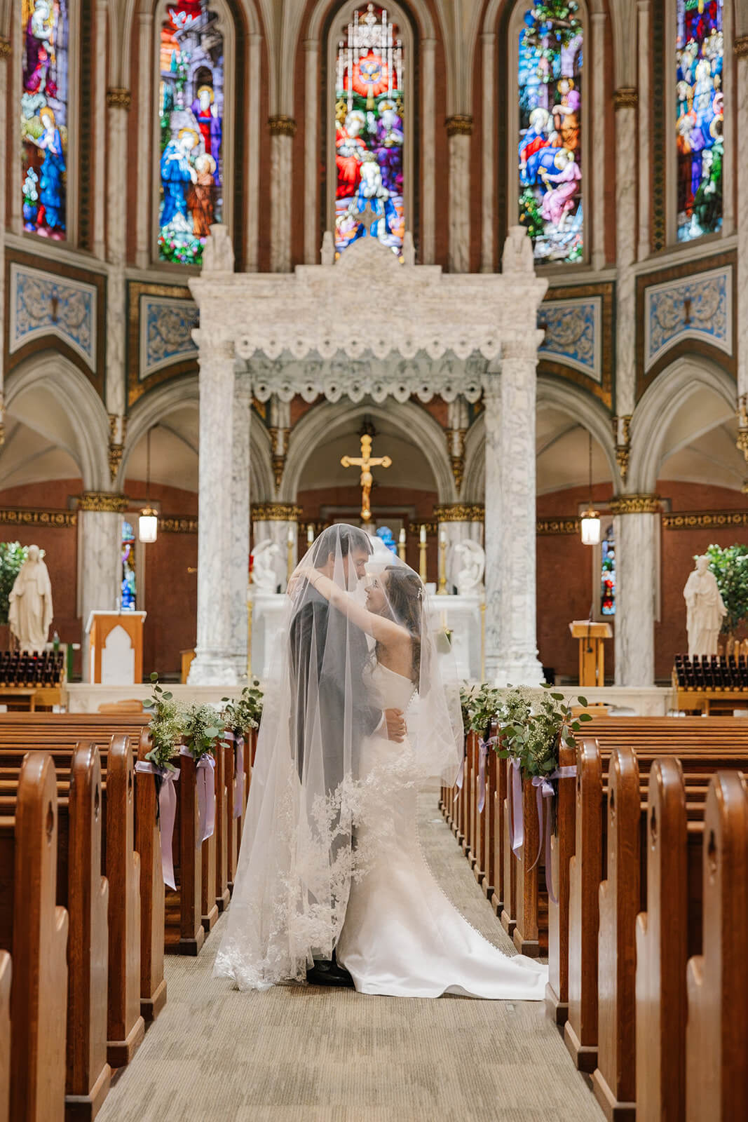 Bride and groom wrapped in bride's cathedral veil after their wedding ceremony