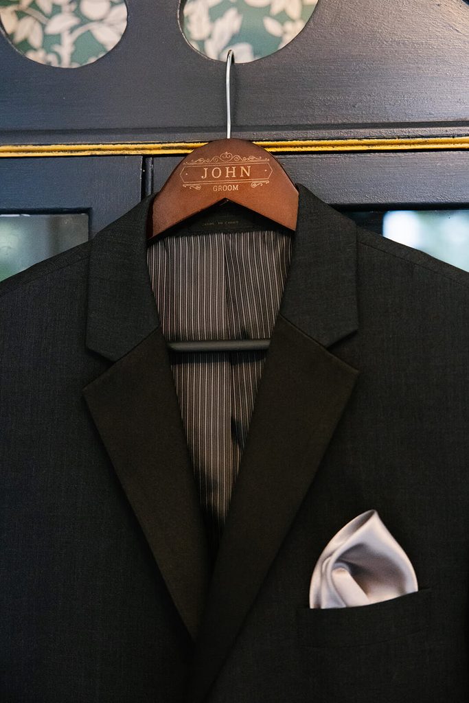 Groom's tux hung on a custom wooden hanger with the name "John"