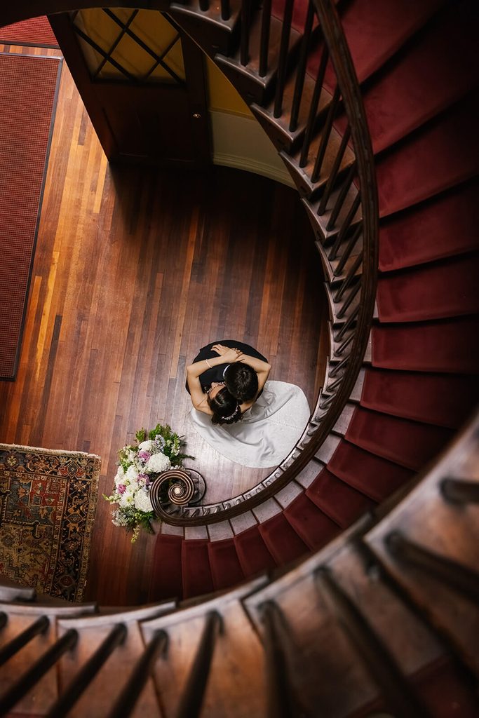 Bride and groom embracing at the bottom of a stunning spiral staircase