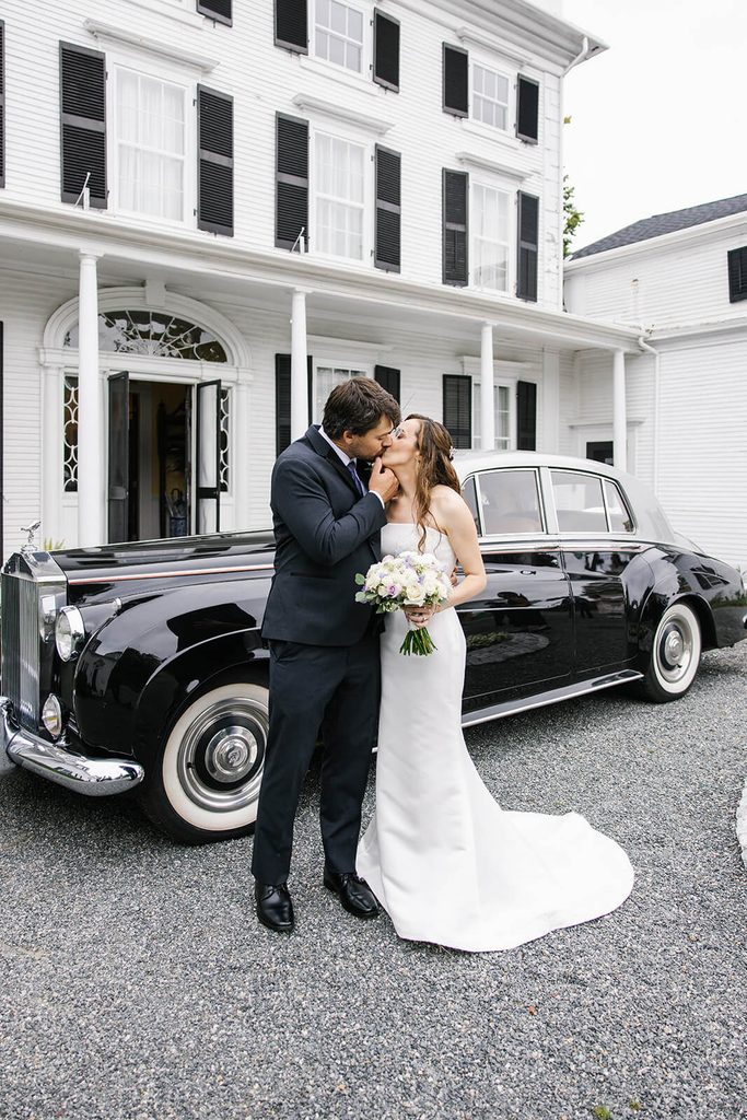 Bride and groom kissing in front of a vintage car parked at their wedding venue, Linden Place