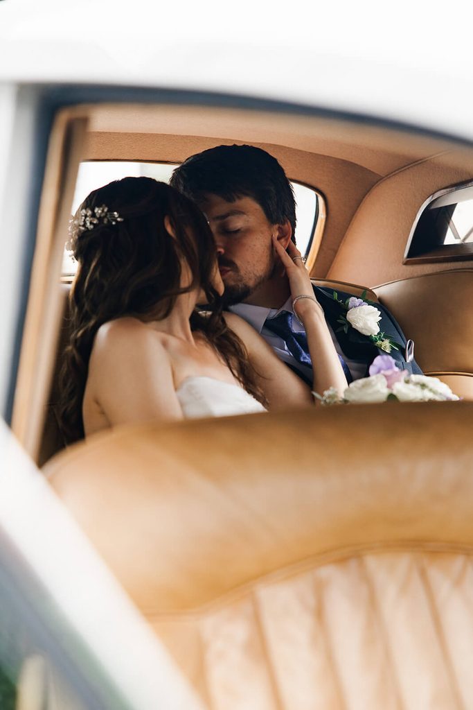 Bride and groom kissing in the back of a vintage car